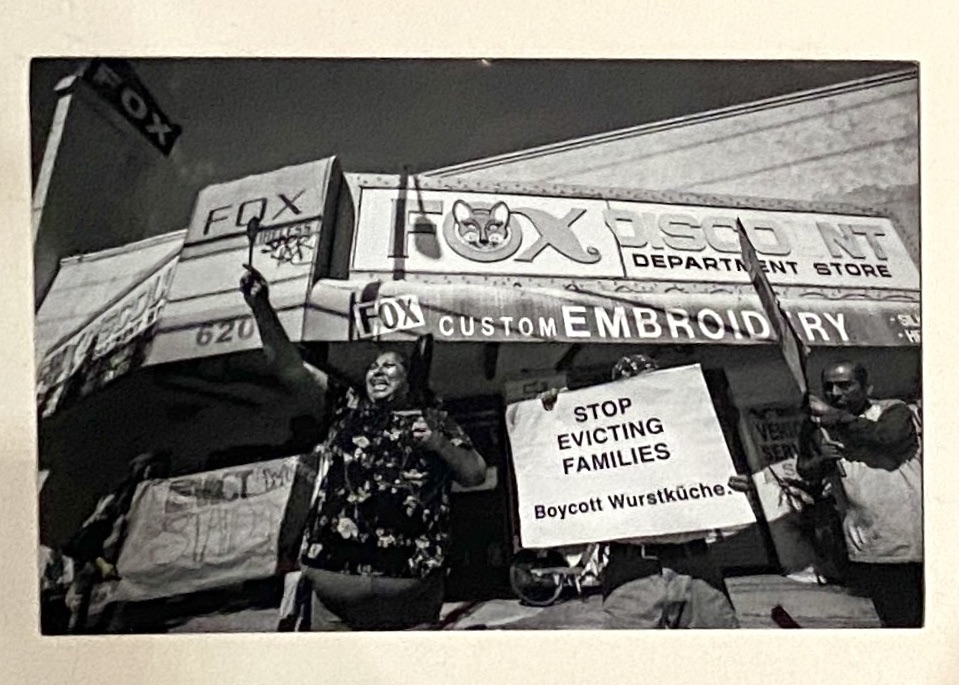 A photograph of protesters outside Venice’s Fox Theater. One holds a sign saying ‘Stop Evicting Families / Boycott Wurstküche'